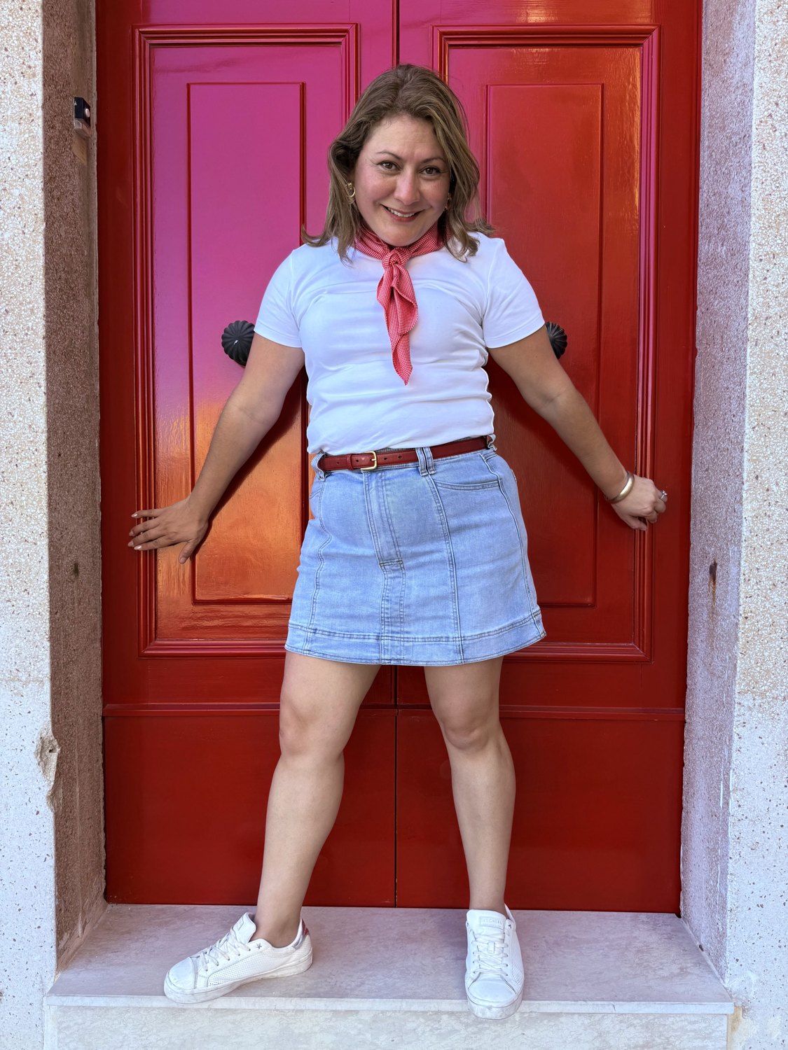 Jessica in a white tee and denim skirt against a bright red door
