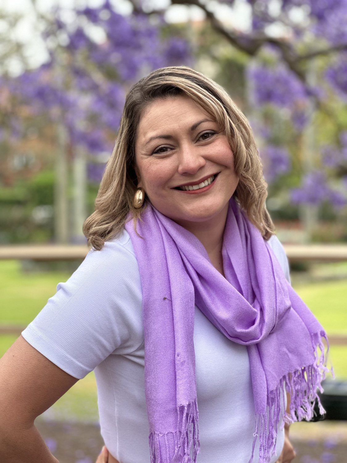 Jessica smiling in a lilac scarf under jacaranda trees