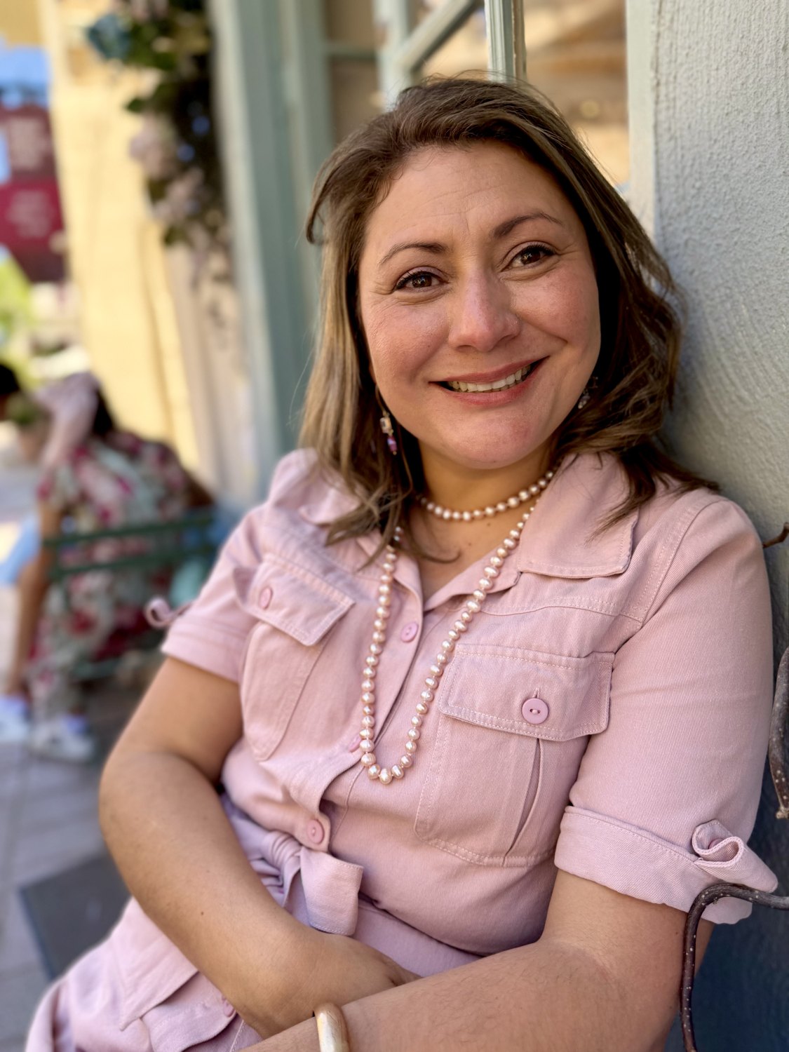Jessica in a pink shirt dress and pearls, smiling