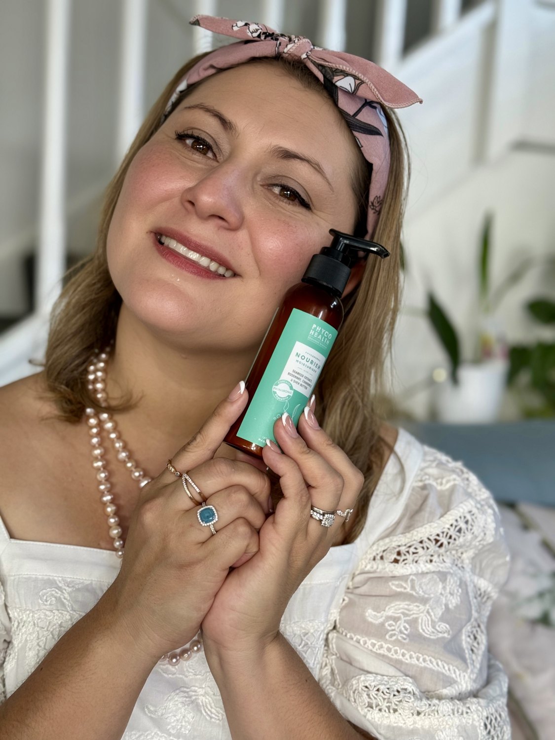 Jessica holding a skincare bottle, wearing pearls and white lace