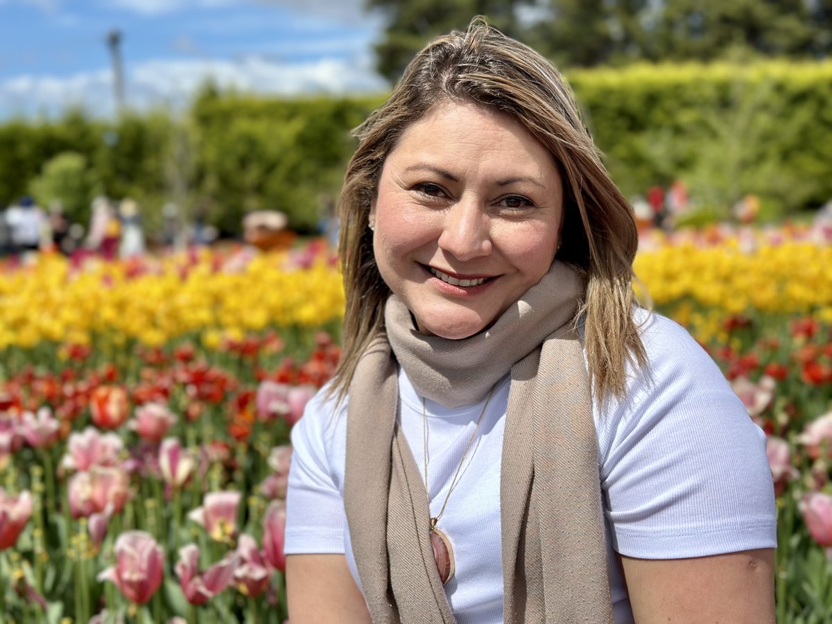 Jessica smiling in a white tee and taupe scarf among tulips